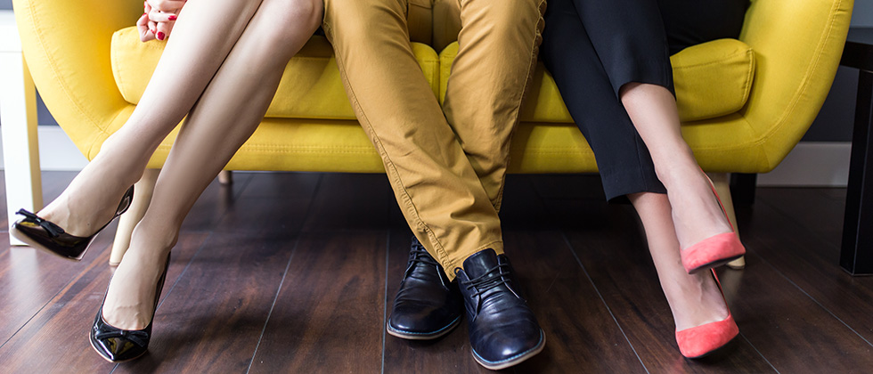 A man sits between two women on a sofa. Only their legs are visible