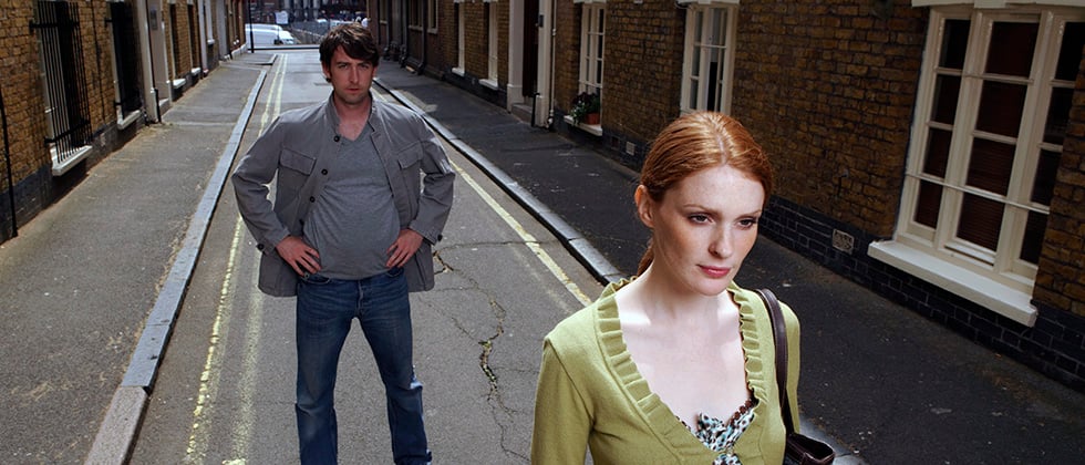 A red-haired woman walks away from a man on a narrow strees