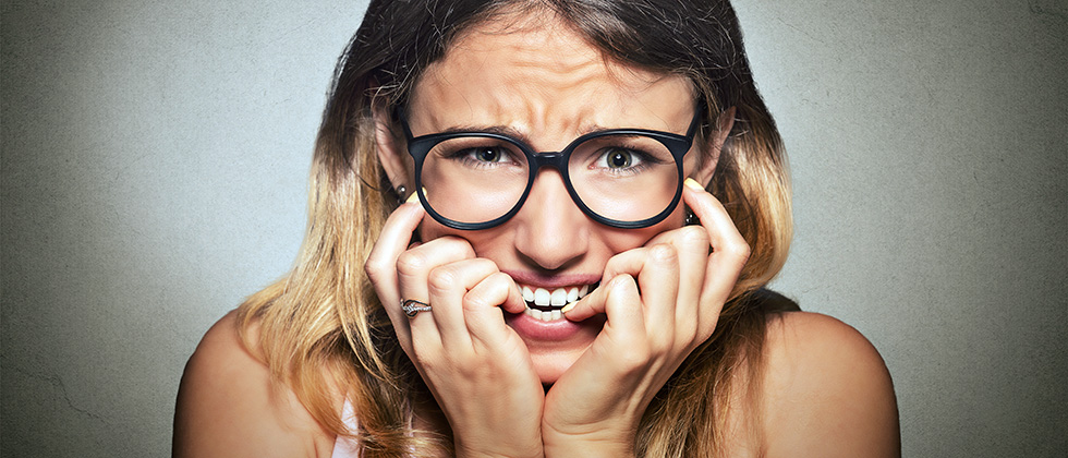 A nervous woman looks to camera, biting her nails