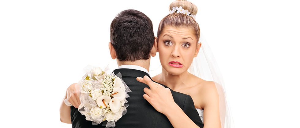 A bride hugs her new husband with fingers crosssed behind his back