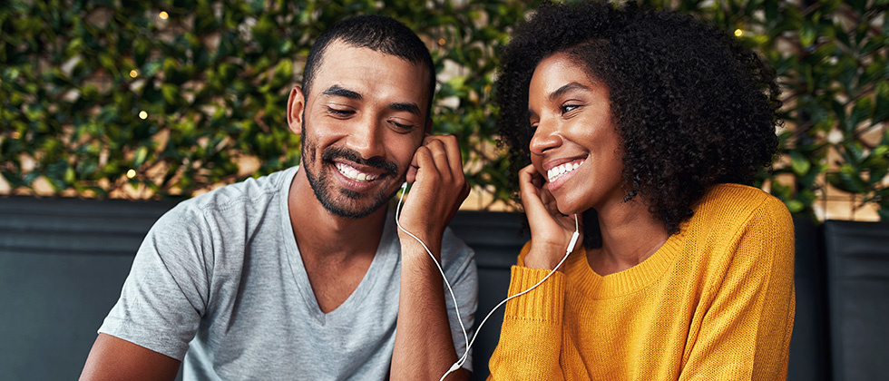 A young couple sit in a café, sharing a set of earphones listening to music