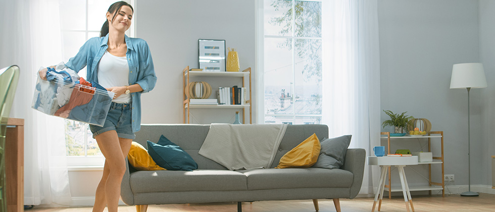 A woman carries a basket of laundry across her living room