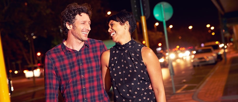 A couple in their 40s walk arm-in-arm along a street at night