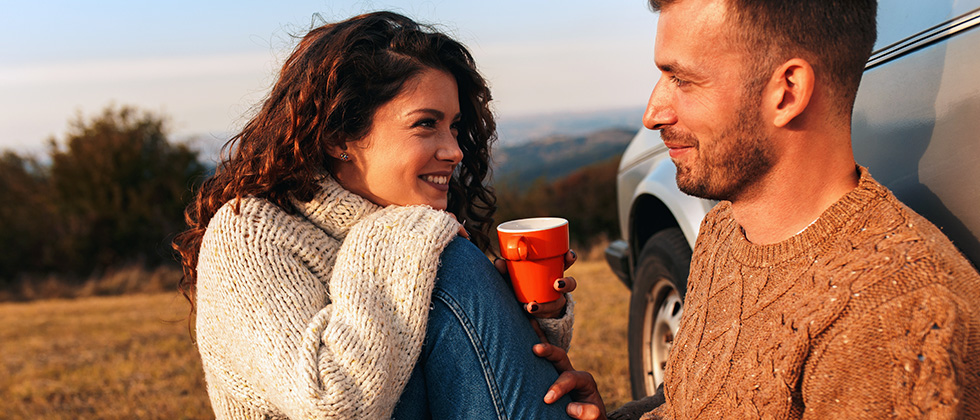 A young couple enjoy a picnic in a field, sitting in front of a car
