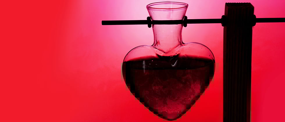 A heart-shaped test tube in a stand against a red background