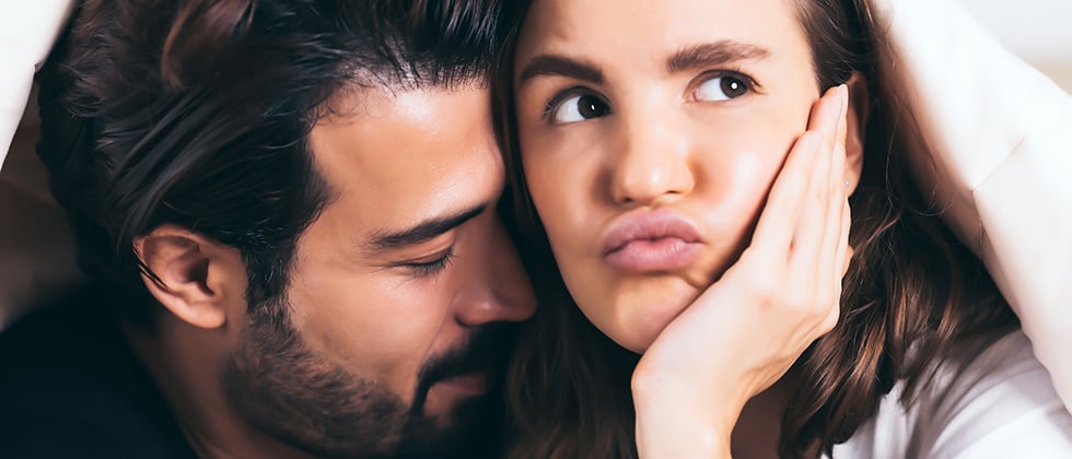 A woman looks bored while her male partner nuzzles her neck