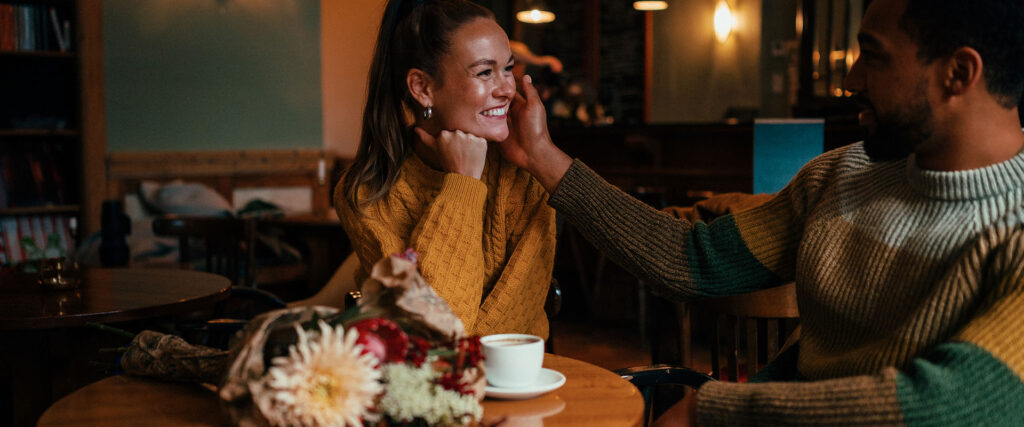 Man and woman in cafe, man caresses her face and she smiles as an example of the question does he like me