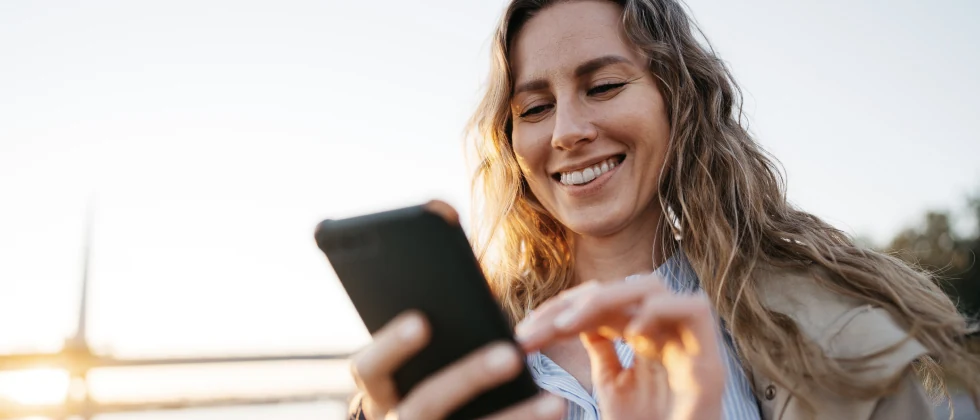 A girl outdoors clicking at her phone, smiling.