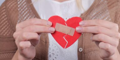 A woman holding a cutout broken heart with a band aid taping it together