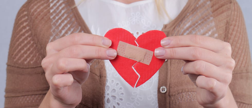 A woman holding a cutout broken heart with a band aid taping it together