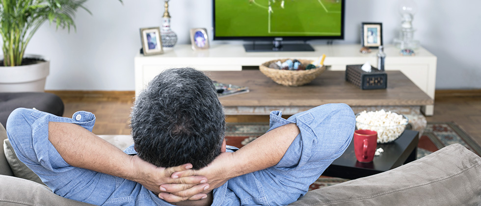 A man reclines on a sofa watching football on TV