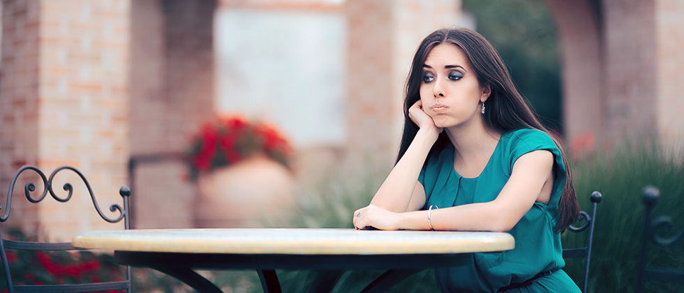 A woman sits on her own at a restaurant table, looking exasperated