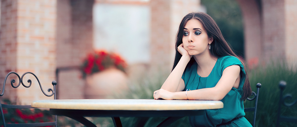 A woman sits on her own at a restaurant table, looking exasperated