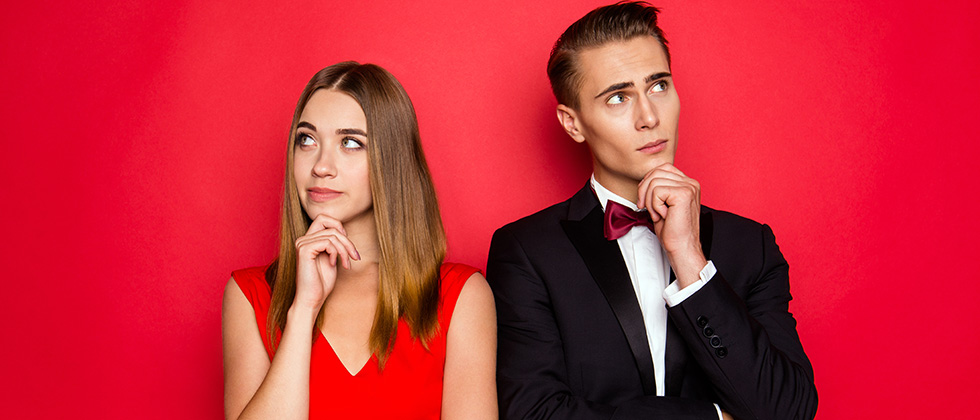 A woman in a red dress and a man in a dinner suit stand shoulder-to-shoulder, but look away from each other