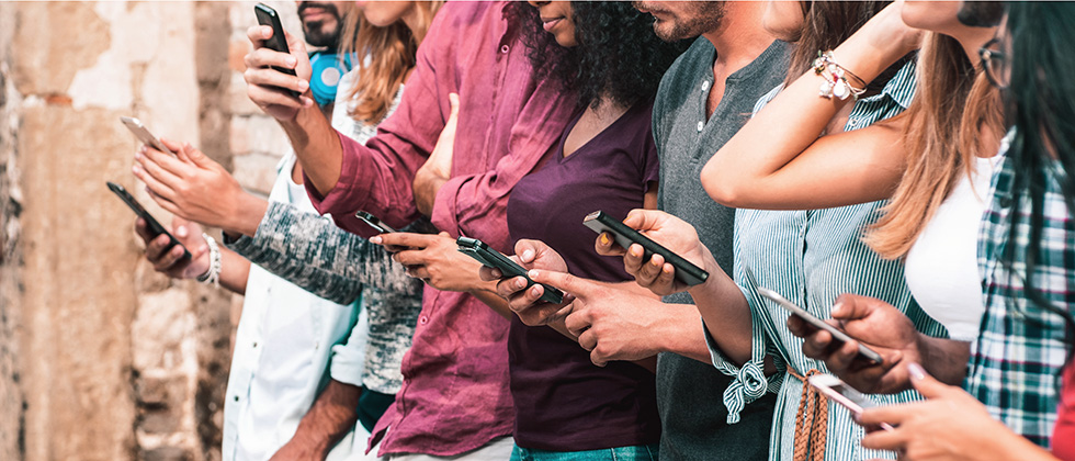A group of people stand in a row, all of them looking at phones