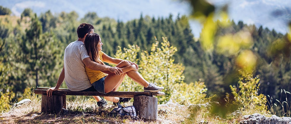 A couple sit on a bench overlooking a scenic view