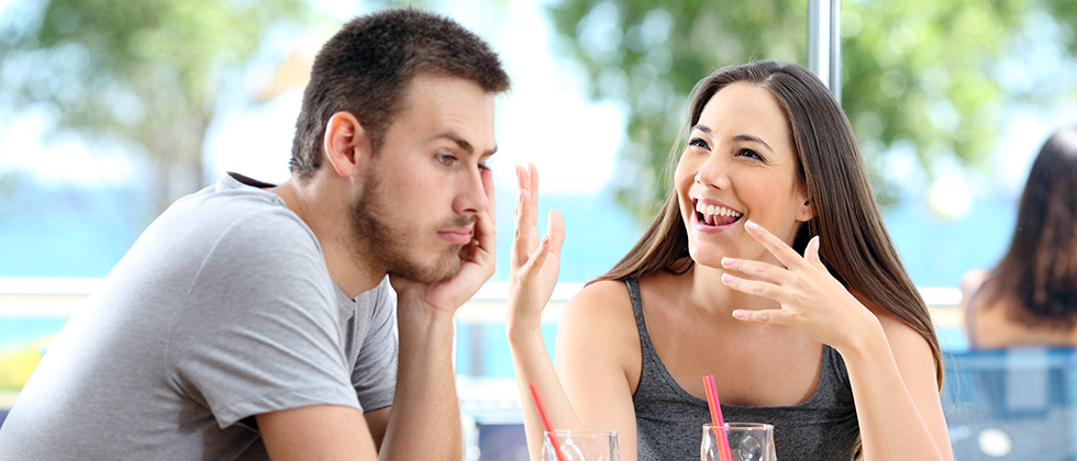 A man looks bored in a restaurant while his partner talks on obliviously