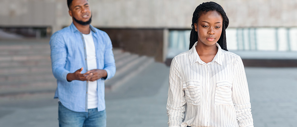 A young woman walks away from her male partner, who beseeches her to stay