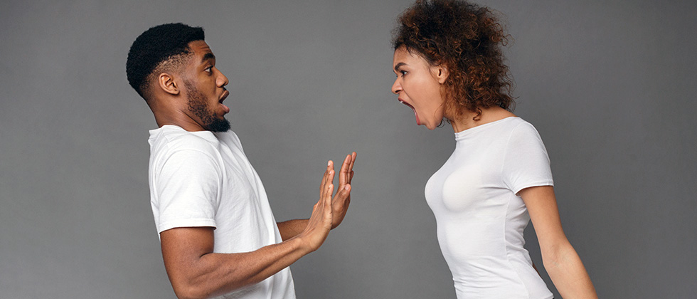 A woman yells angrily in the face of a man, who backs away in surprise
