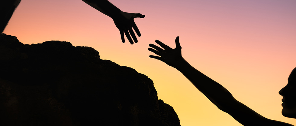 Two figures in silhouette reach their hands towards each other