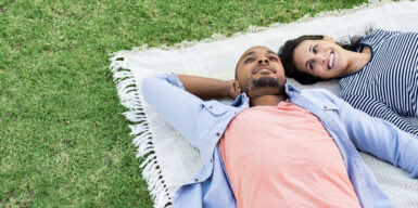 Interracial couple laying together on a picnic blanket in a field