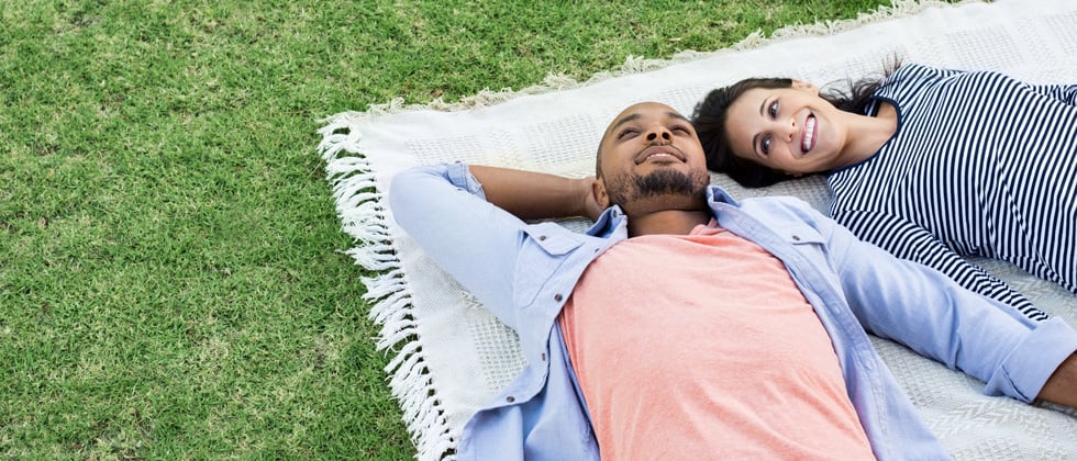 Interracial couple laying together on a picnic blanket in a field