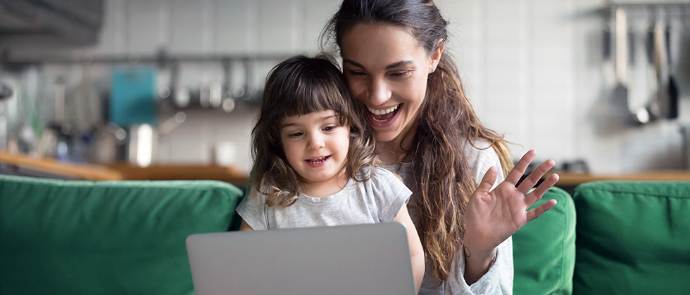 A young girl sits on her mother's lap as they both look at a laptop screen