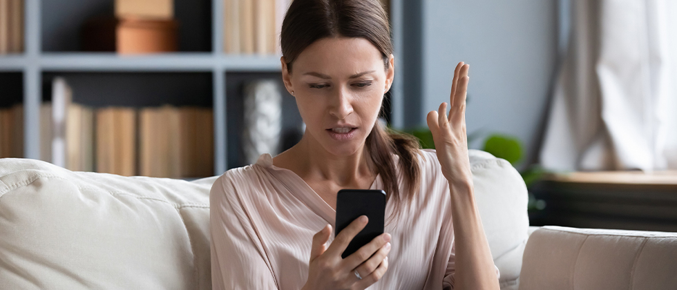 A woman sits on the sofa looking angrily at her phone