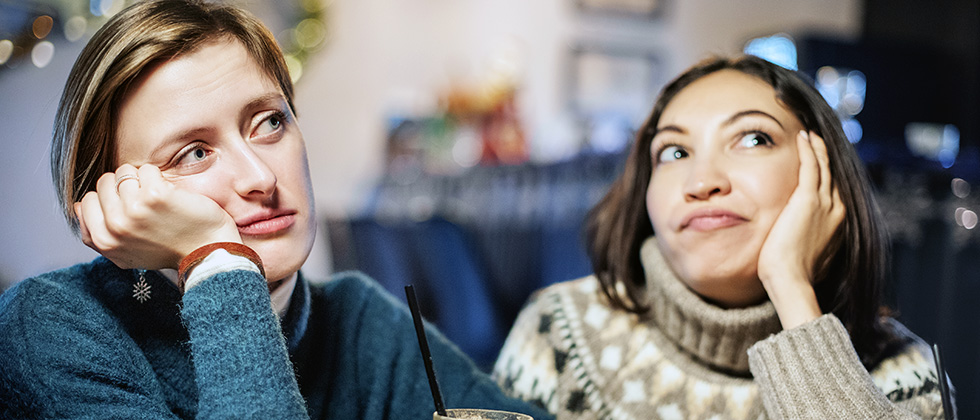 Two women on a date sit at a bar looking bored