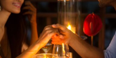 Couple on a romantic date holding hands above a candle lit dinner