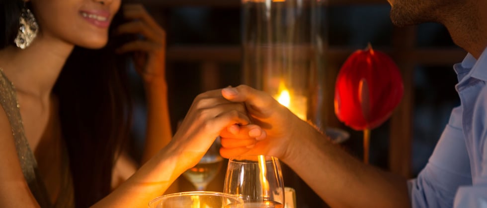 Couple on a romantic date holding hands above a candle lit dinner