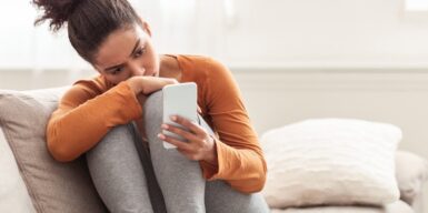 A woman curled up on the couch looking into her phone concerned