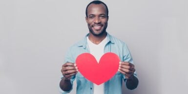 A man standing holding up a cutout heart & smiling