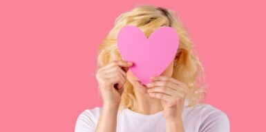 A woman holding a pink cutout heart over her face
