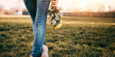 Someone walking in an empty grass field holding yellow roses