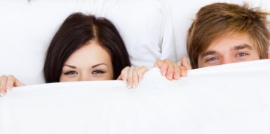 A couple in bed together with the sheets partly covering their faces