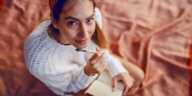 A young woman sitting on a picnic blanket writing in a journal