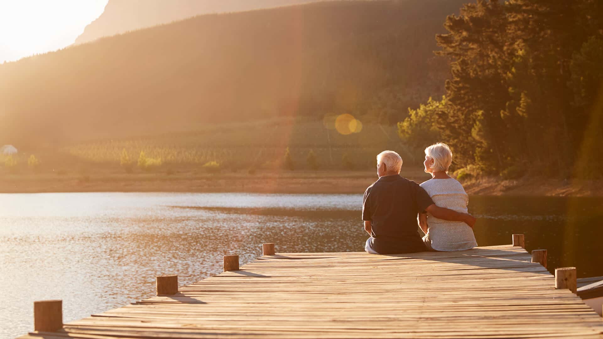 Widowed dating in Australia symbolized by a man and woman sitting next to each other on a dock end enjoy the sundowner