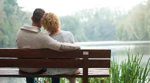 A couple relaxing on a bench next to a lake and enjoying quiet moments of nature.