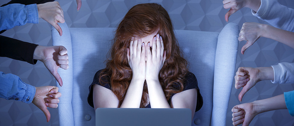A woman sits in front of a compute with her head in her hands