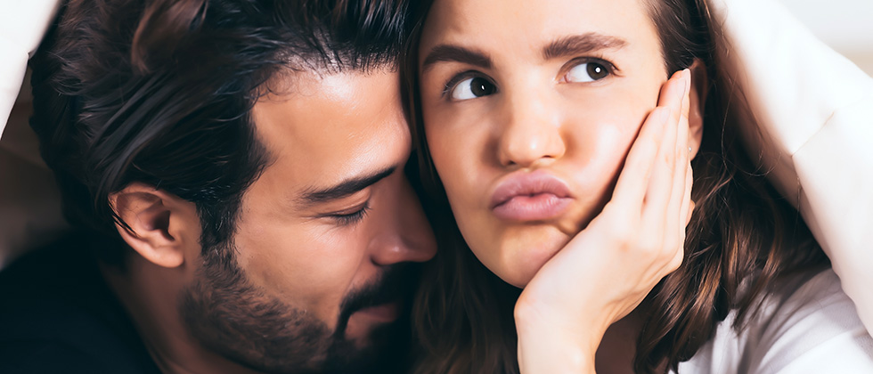 A woman looks bored while her male partner nuzzles her neck