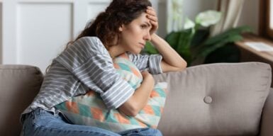 Concerned woman sitting alone on the couch holding a pillow