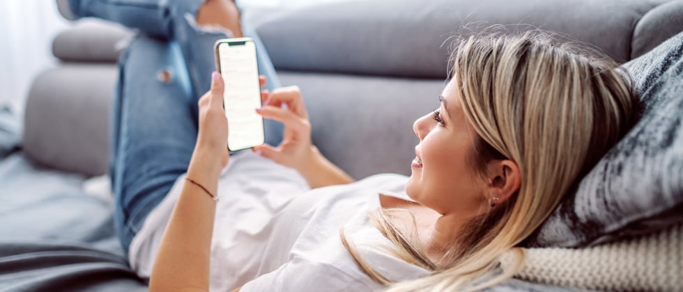 Woman laying on her couch casually while holding her phone