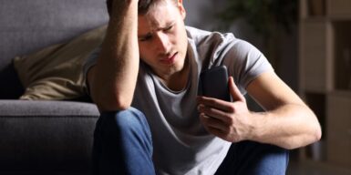 Worried and upset man sitting on the ground looking at his phone
