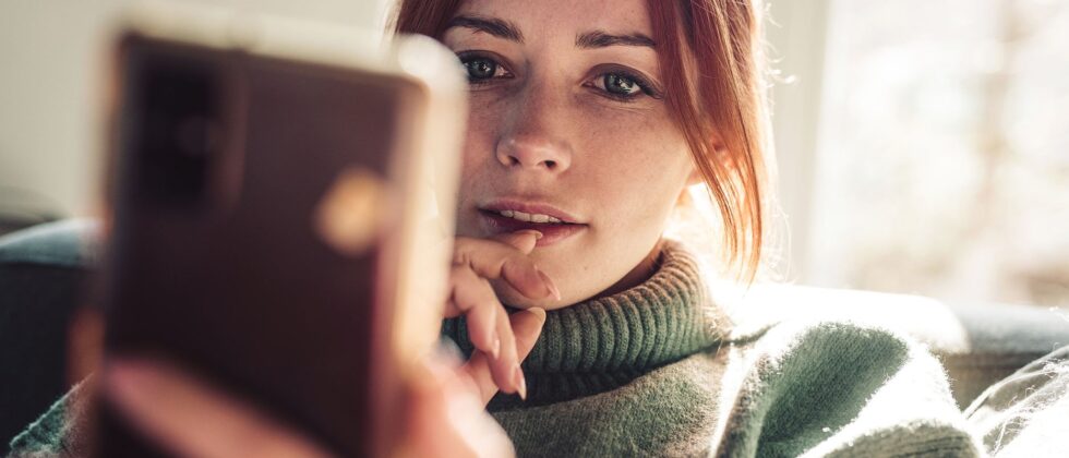 Woman looks at her cell phone and wonders to call or text