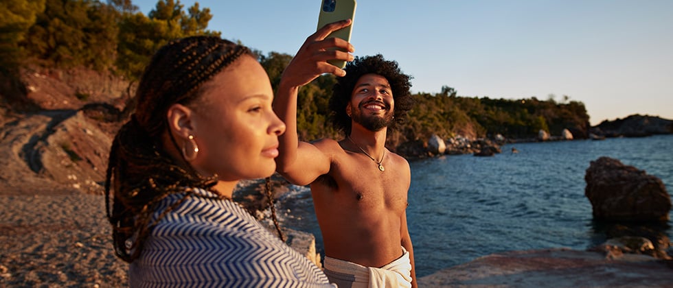 Man and woman on beach and man has mobile phone in hand as example of is sexting cheating