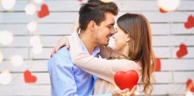 A couple hugging and kissing in the middle of string lights and hearts