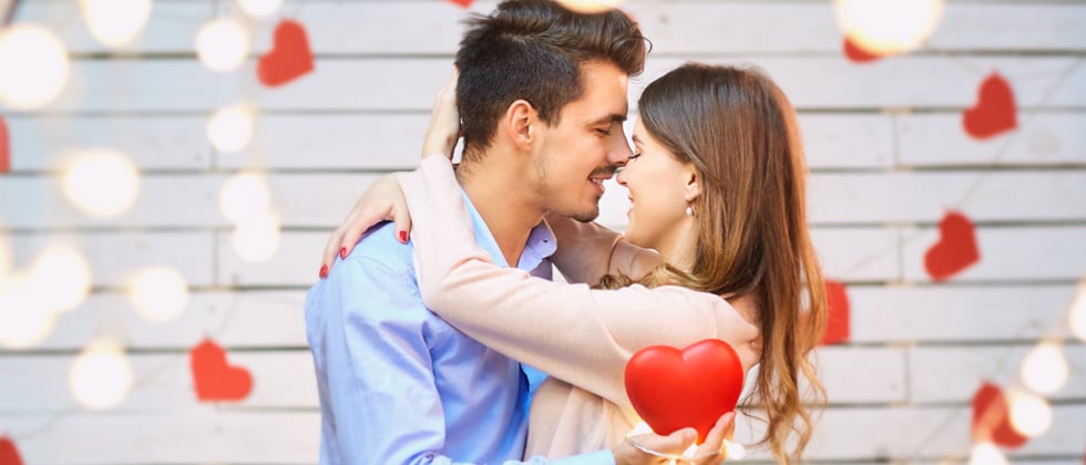 A couple hugging and kissing in the middle of string lights and hearts