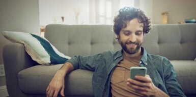 Man sits on the sofa with his cell phone and informs himself about eharmony settings