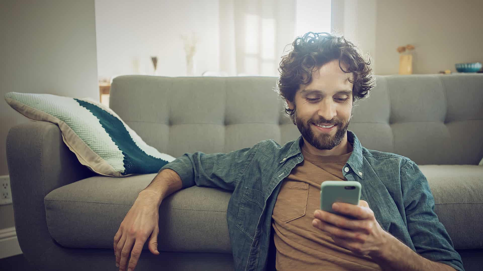 Man sits on the sofa with his cell phone and informs himself about eharmony settings